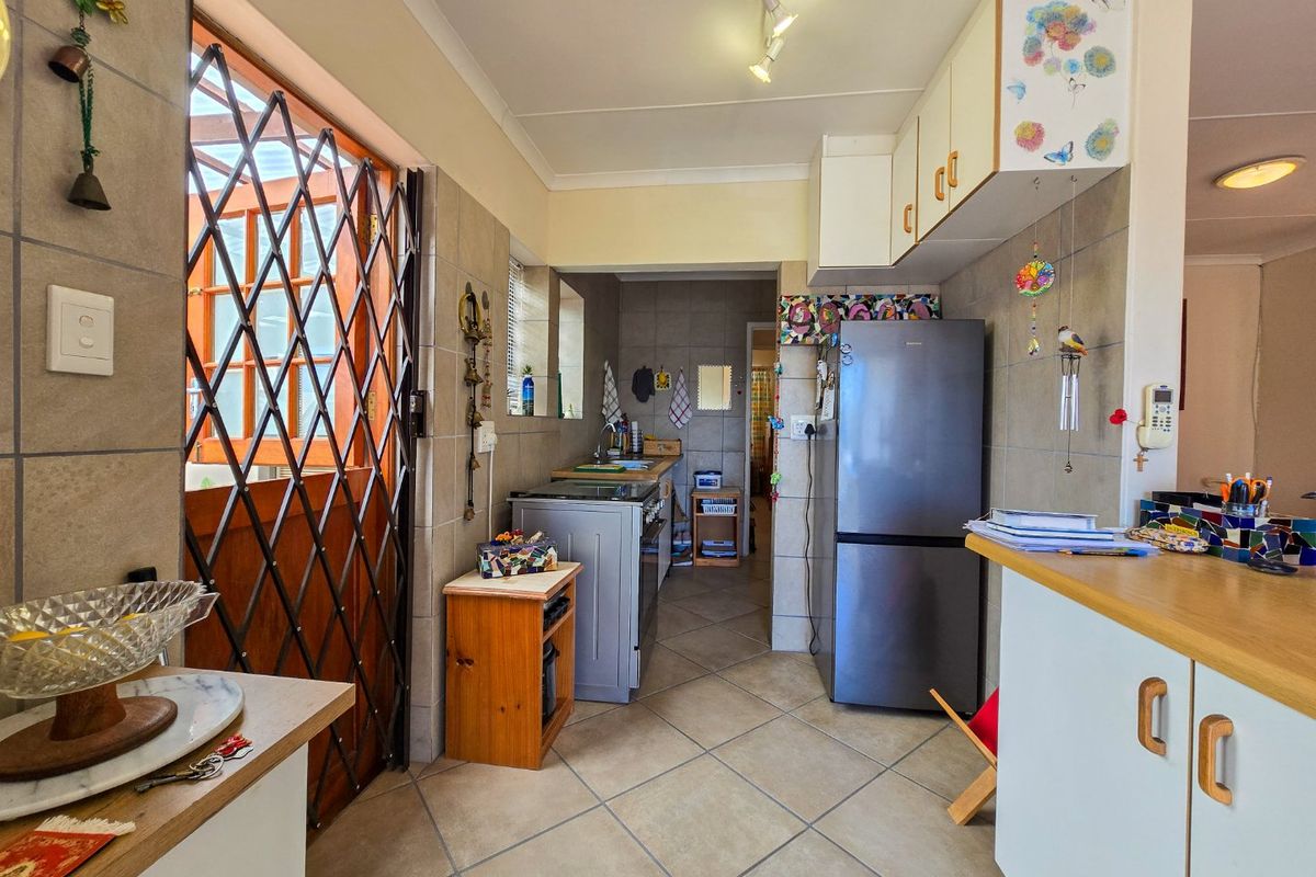 A functional kitchen featuring tiled flooring, wall-mounted cabinetry, and laminate countertops, with direct access to an outdoor area through a security gate.