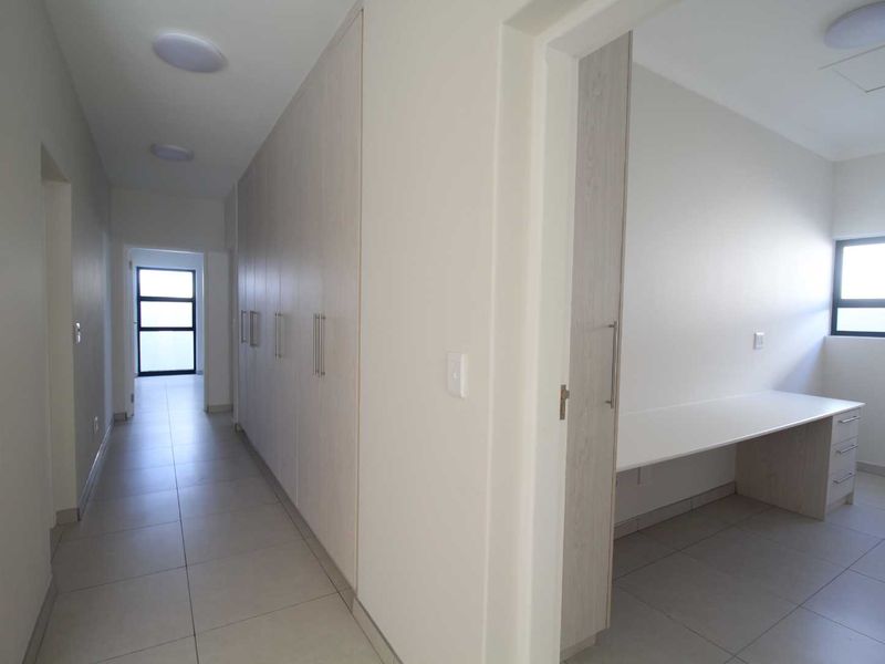 A bright, modern hallway featuring extensive built-in storage cupboards and a dedicated built-in desk area, finished with neutral floor tiles.
