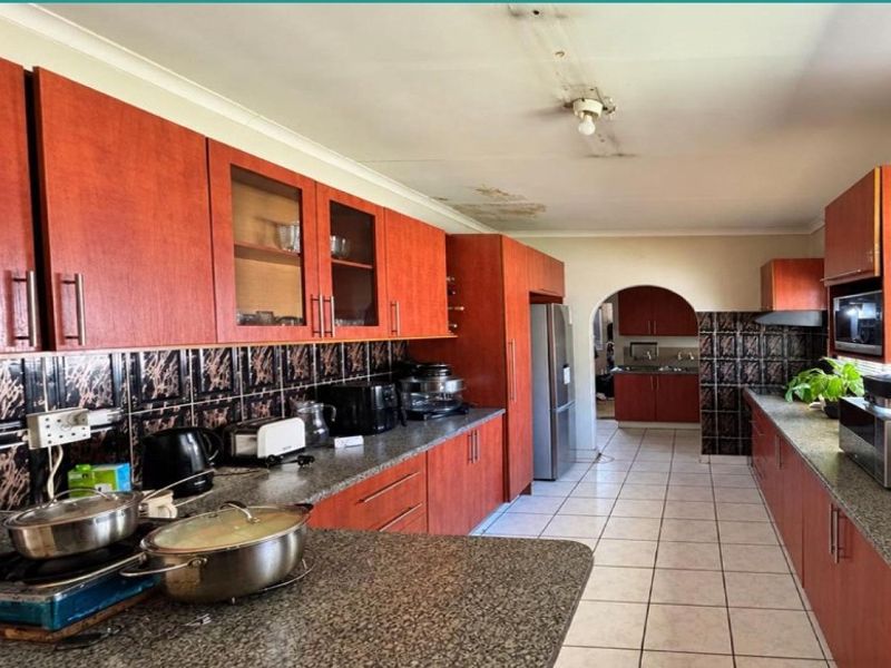 Spacious kitchen featuring wood-finish cabinetry, granite countertops, and a tiled backsplash, with an adjoining scullery area visible through the archway.