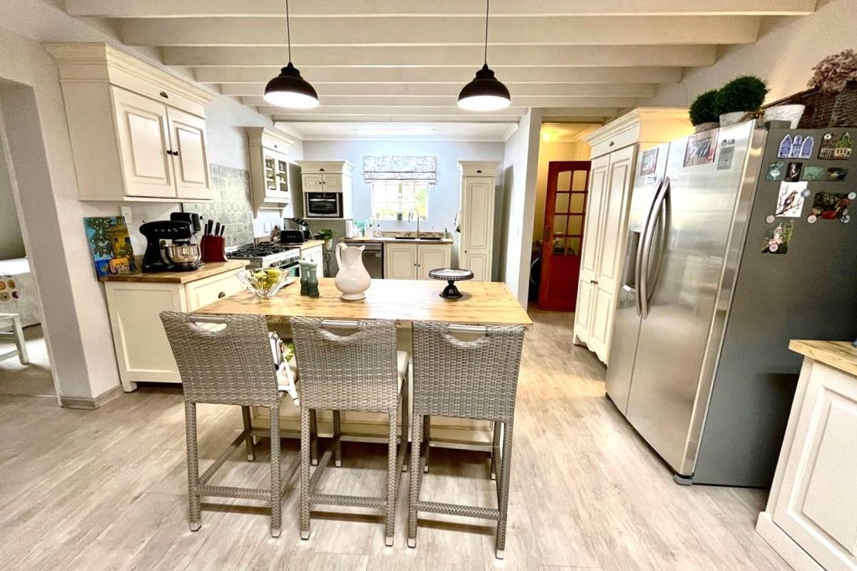 A well-appointed kitchen featuring cream cabinetry, a central wooden island with breakfast seating, exposed ceiling beams, and modern stainless steel appliances.