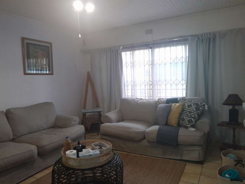 A living room featuring tiled flooring, a ceiling fan, and a window fitted with a security gate.