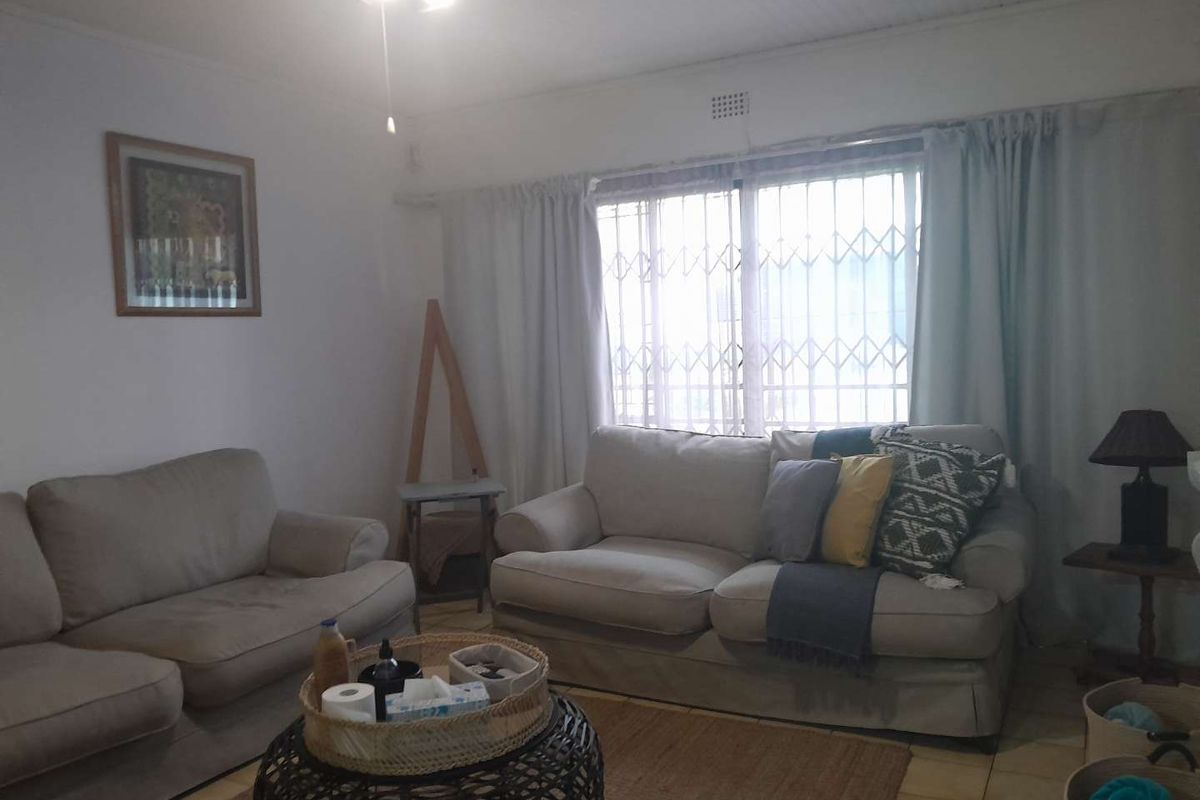 A living room featuring tiled flooring, a ceiling fan, and a window fitted with a security gate.