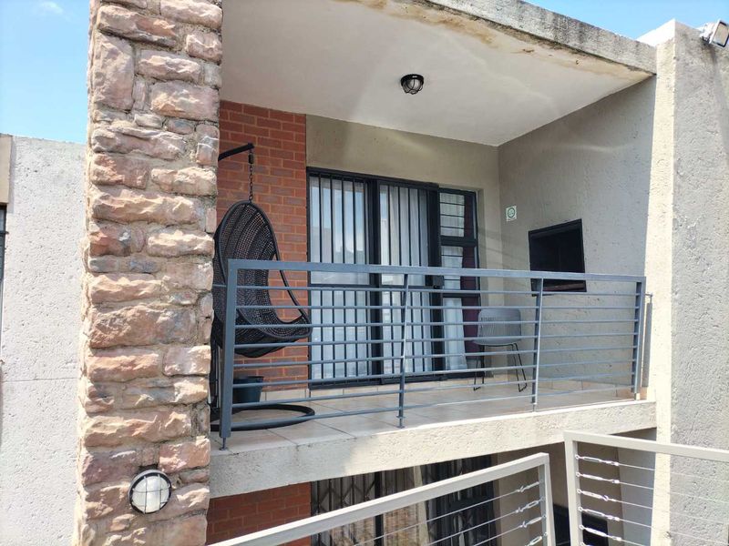 A balcony featuring a built-in braai, stone and brick accents, and a metal balustrade, showing signs of weathering on the ceiling.