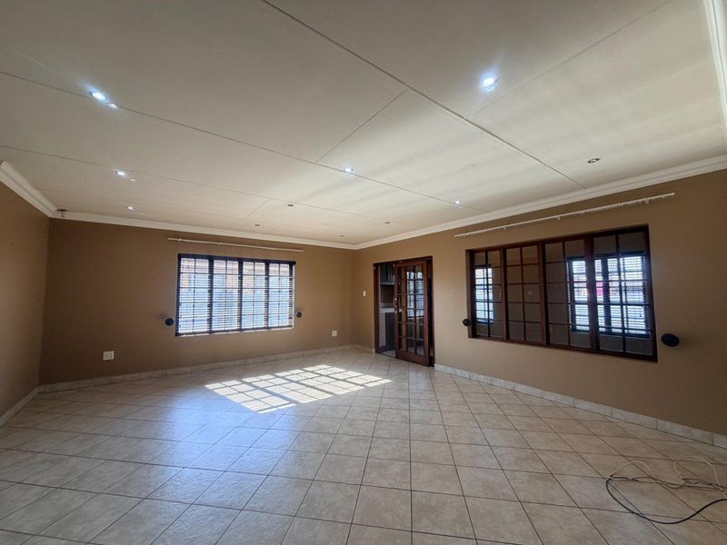 A spacious, empty living room featuring neutral-toned walls, tiled flooring, recessed lighting, and classic timber-framed windows and doors.
