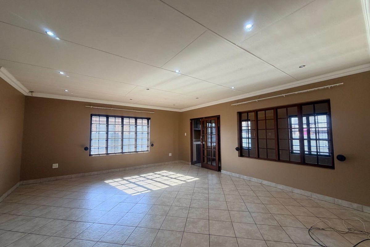 A spacious, empty living room featuring neutral-toned walls, tiled flooring, recessed lighting, and classic timber-framed windows and doors.