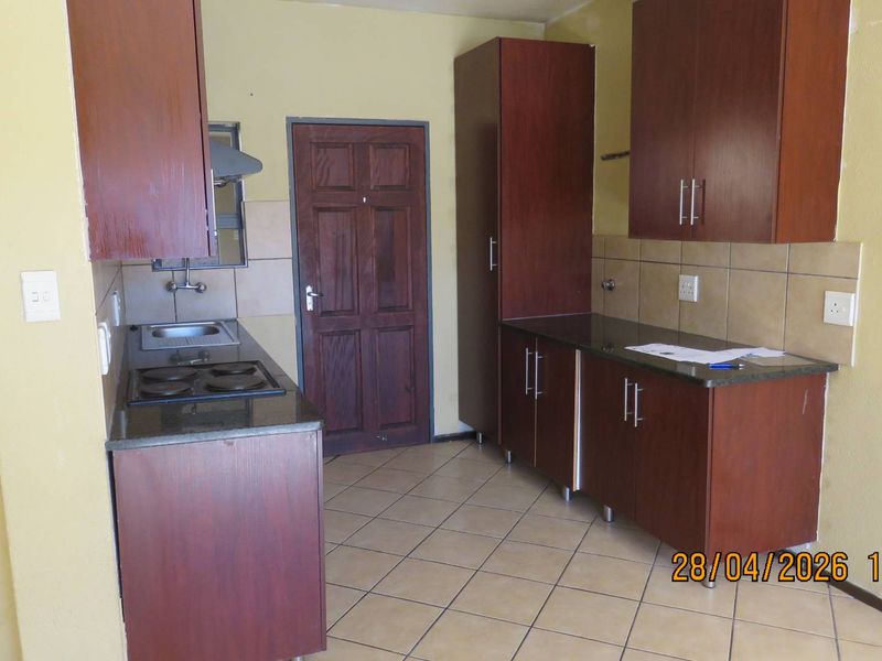 A functional kitchen featuring dark wood cabinetry, granite countertops, a built-in hob, and tiled flooring, offering a practical layout for daily use.