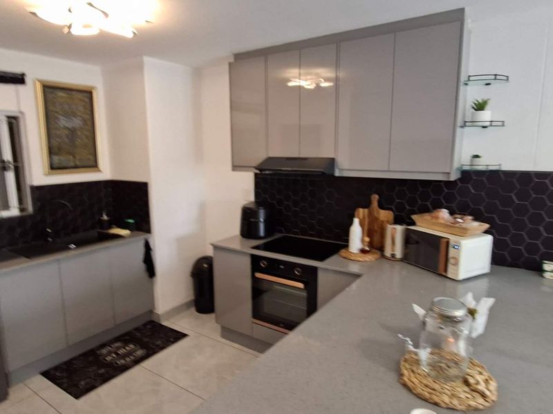 Modern kitchen featuring grey cabinetry, stone countertops, black hexagonal tile backsplash, integrated oven, hob, and extractor fan with tiled flooring.
