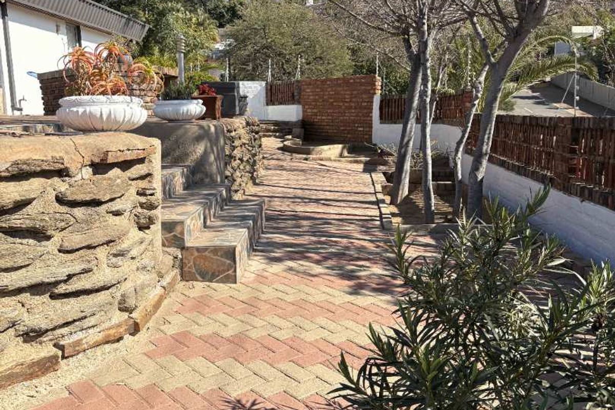 A paved outdoor area featuring stone retaining walls, brick boundary fencing, and tiered steps leading through the garden space.
