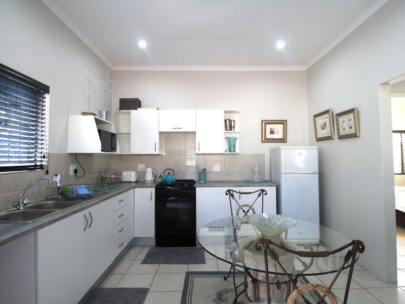 A functional kitchen featuring white cabinetry, laminate countertops, a tiled backsplash, and a freestanding oven, with direct access to an adjacent bedroom.