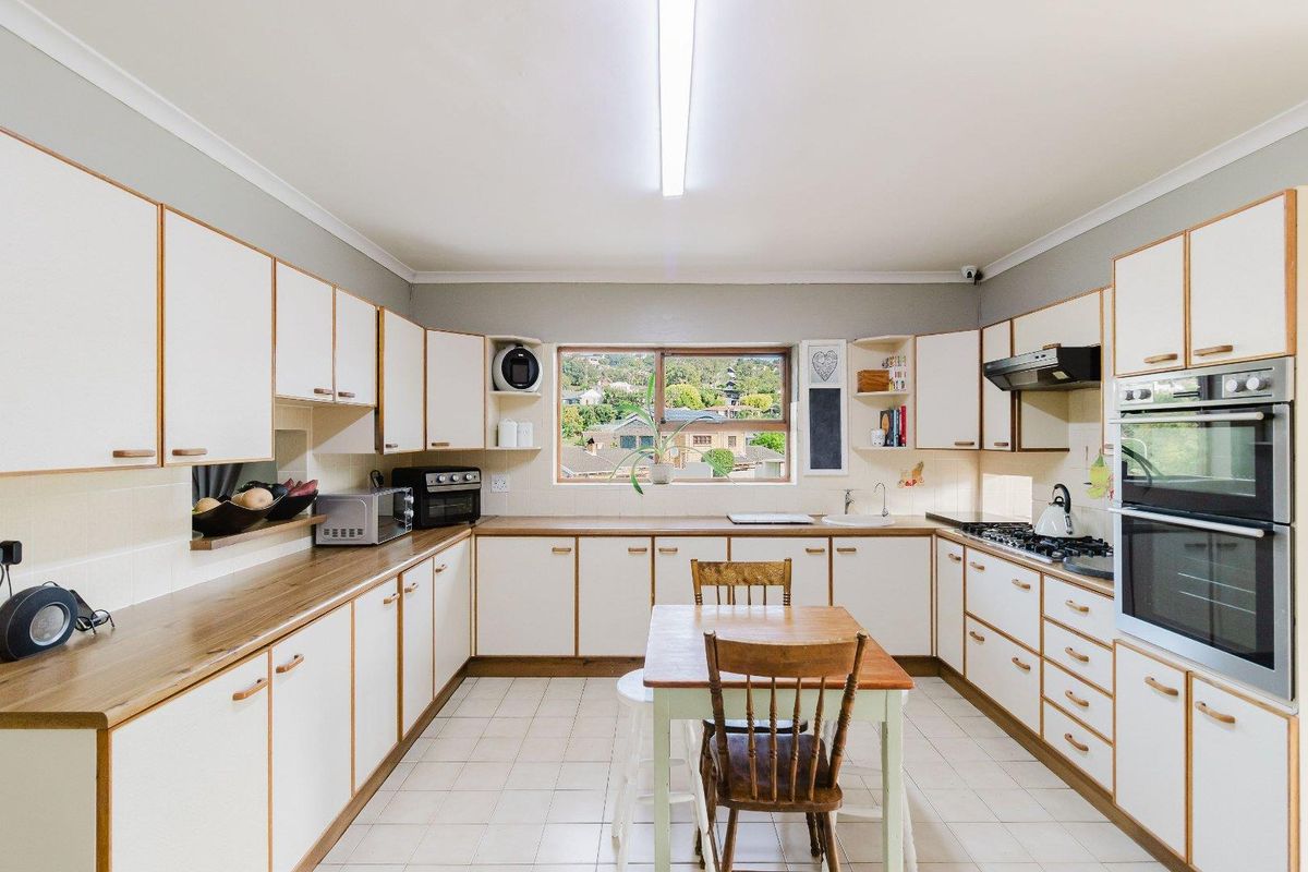 A functional kitchen featuring white cabinetry with wood trim, tiled flooring, a built-in oven, gas hob, and an extractor fan with a window view.