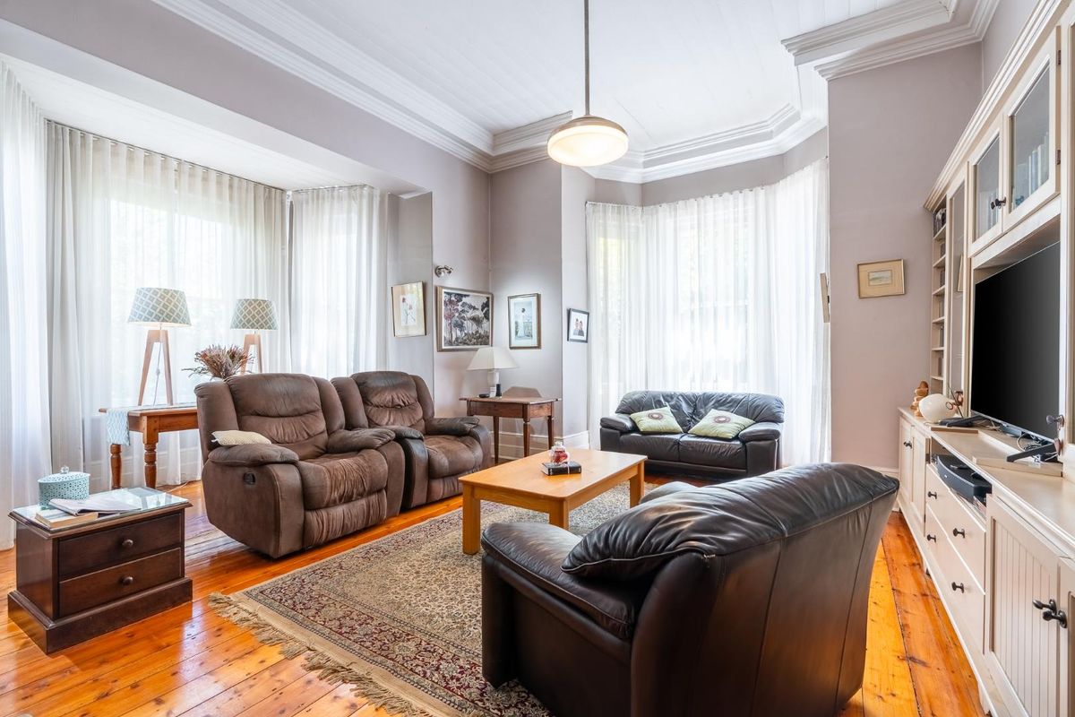 Spacious living room featuring polished hardwood floors, elegant crown molding, and large bay windows that provide ample natural light.