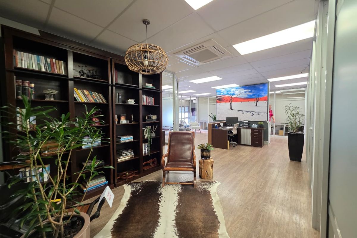 Modern office space featuring glass partitions, suspended ceilings with recessed lighting, ducted air conditioning, and durable wood-look flooring.
