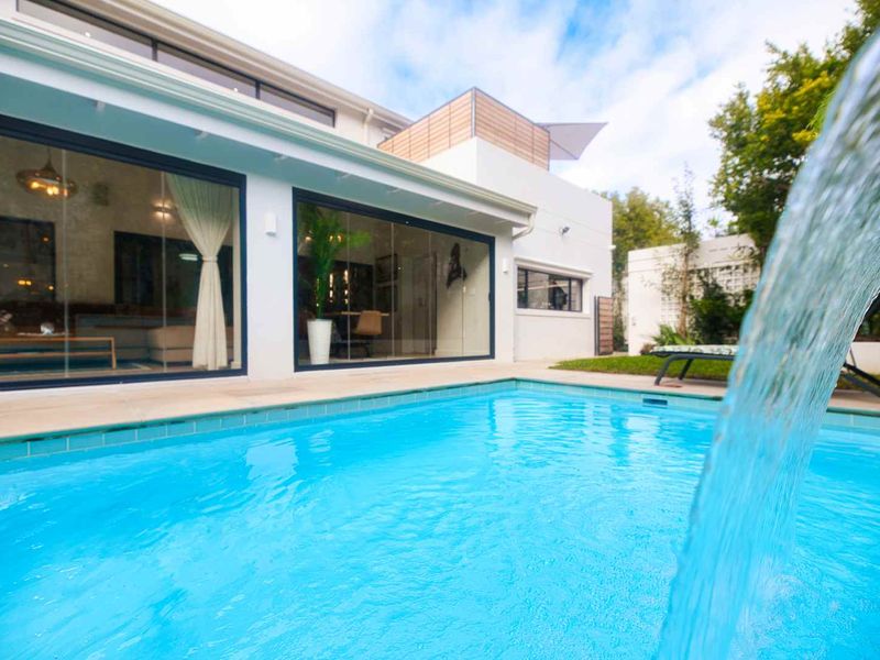 A modern swimming pool area featuring a water feature, tiled decking, and large sliding glass doors providing seamless indoor-outdoor flow.