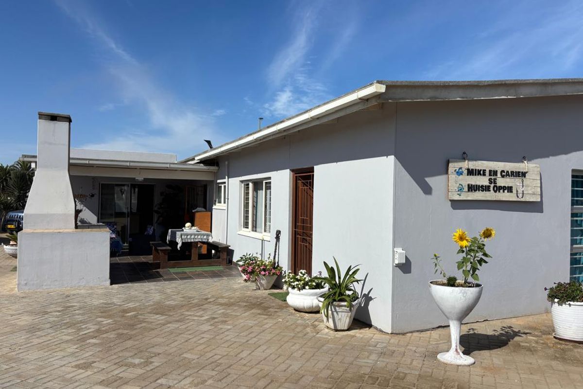 Rear exterior view of the house featuring a paved patio area with a built-in outdoor fireplace and covered entertainment space.