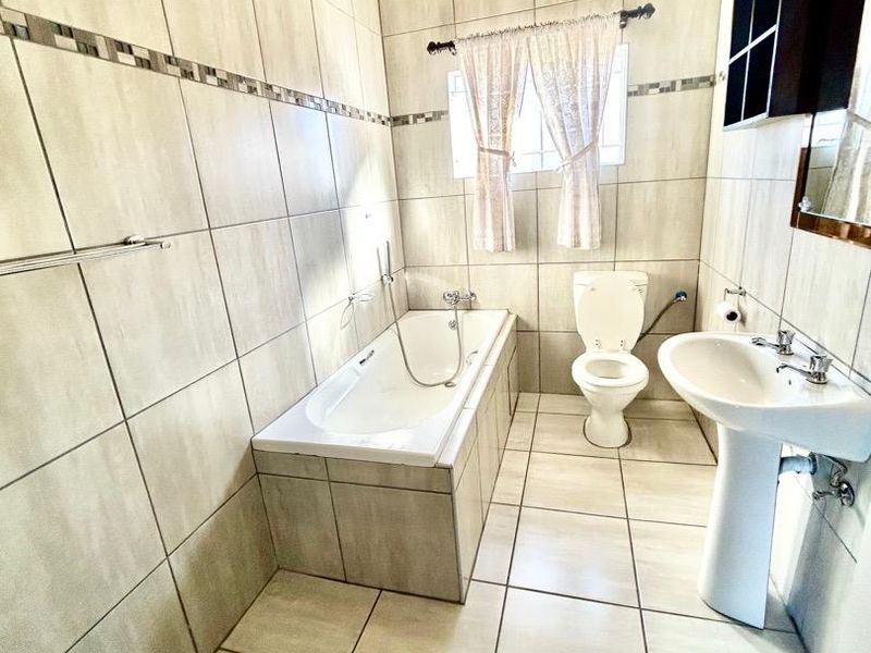 A functional bathroom featuring full-height wall tiling, a built-in bathtub, a pedestal basin, and a standard toilet.