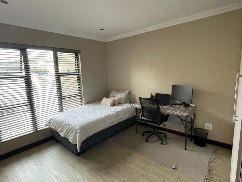 A well-lit bedroom featuring modern laminate flooring, recessed downlighting, and venetian blinds, offering a neutral and functional living space.