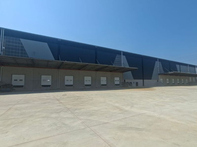 Industrial warehouse exterior featuring multiple loading docks with roller shutter doors, a large concrete yard, and modern metal cladding.