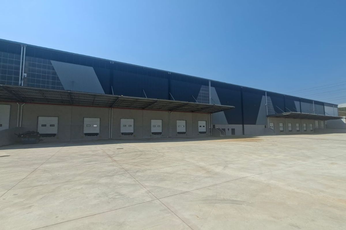 Industrial warehouse exterior featuring multiple loading docks with roller shutter doors, a large concrete yard, and modern metal cladding.
