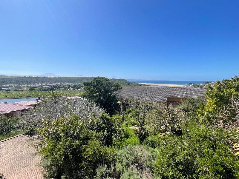 Elevated view overlooking the surrounding landscape, coastal area, and ocean, featuring established greenery and a glimpse of a residential tiled roof.