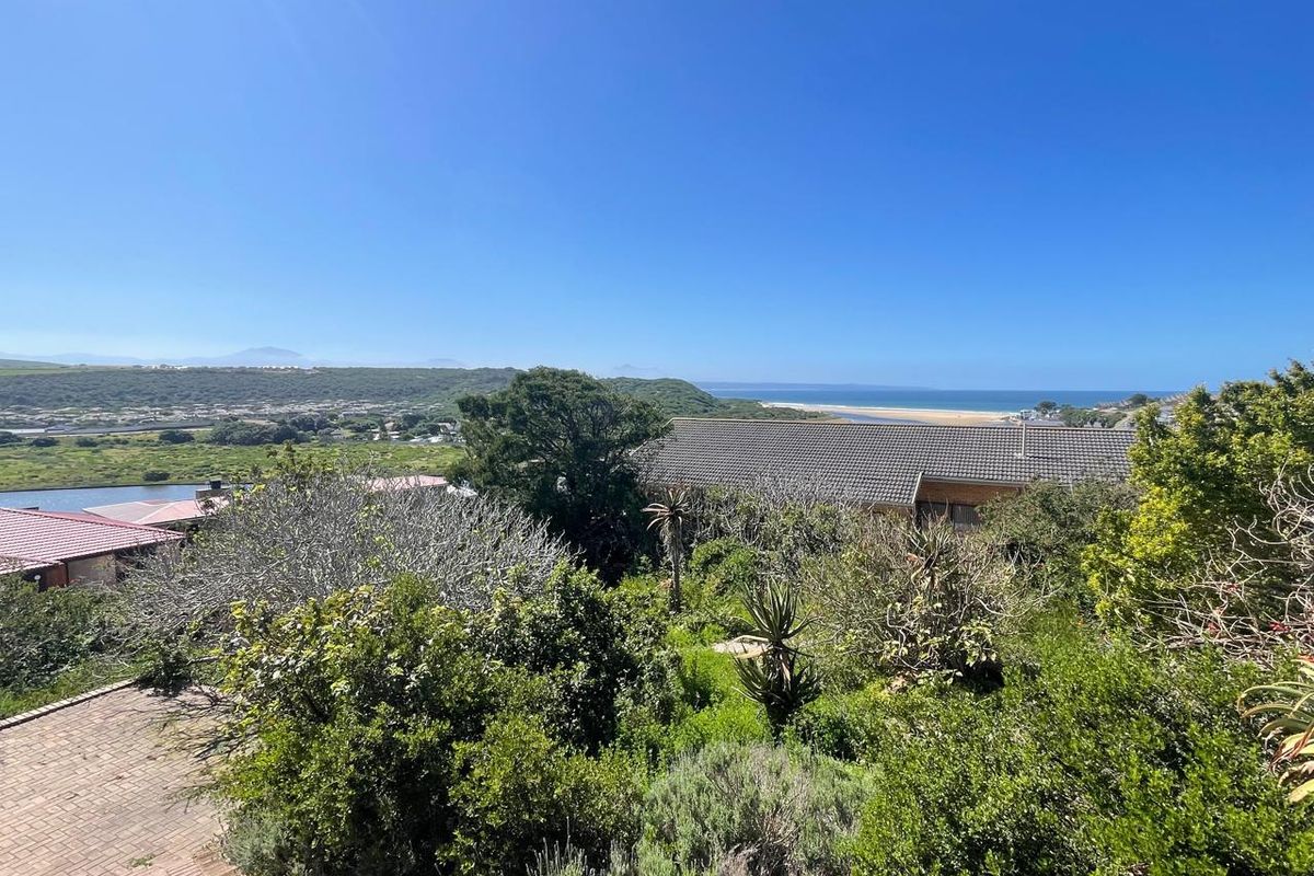 Elevated view overlooking the surrounding landscape, coastal area, and ocean, featuring established greenery and a glimpse of a residential tiled roof.