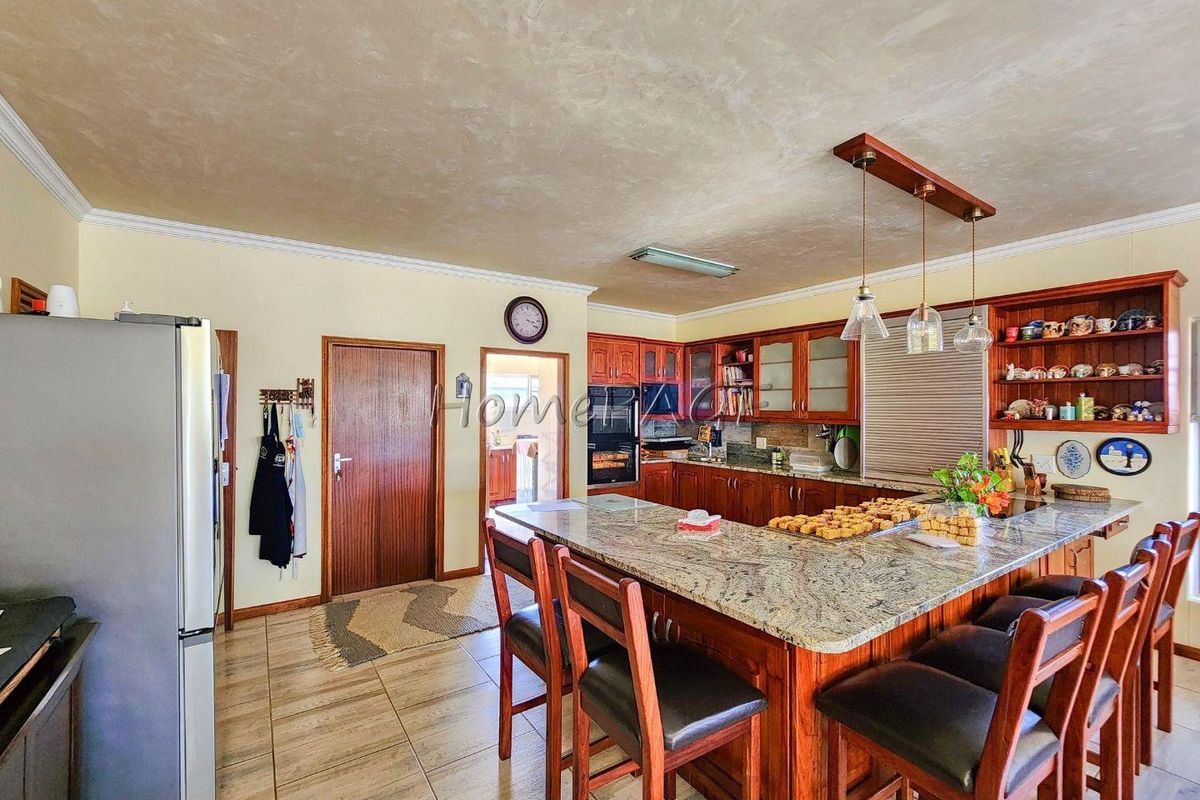 Spacious kitchen featuring wooden cabinetry, granite countertops, a large central island with breakfast bar seating, and tiled flooring.