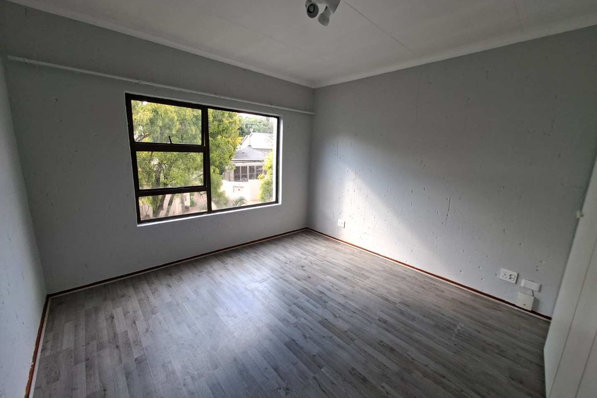 An empty bedroom featuring grey laminate flooring, neutral walls, and a large window providing natural light.
