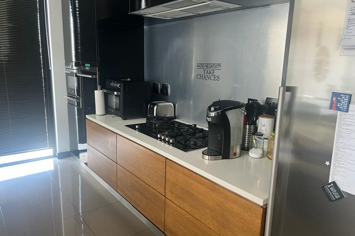Modern kitchen featuring sleek wood-grain cabinetry, white stone countertops, a stainless steel splashback, and integrated built-in oven and gas hob.