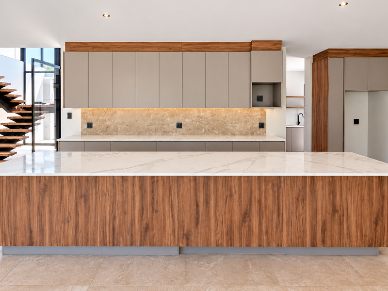 Modern kitchen featuring a large island with stone countertop, sleek cabinetry, floating shelves, and an adjacent floating staircase in a bright, open-plan space.