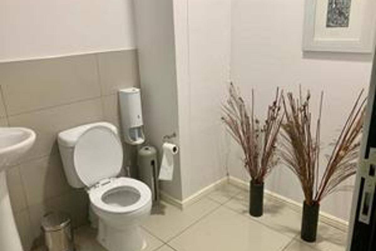 A clean and functional bathroom featuring a pedestal sink, a standard toilet, and neutral floor tiling.