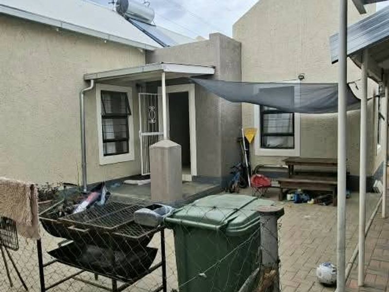 Rear exterior view of the property featuring a paved patio area, solar water heater, and security gate access.