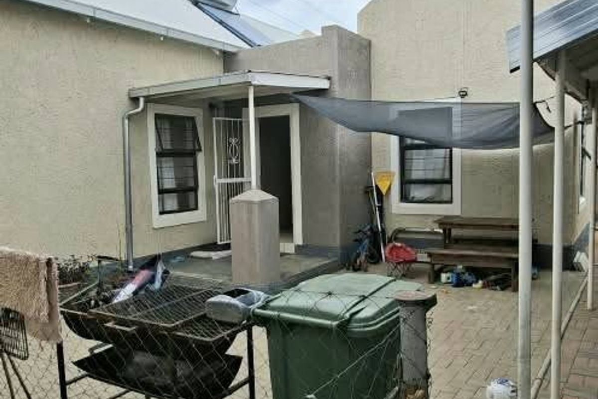 Rear exterior view of the property featuring a paved patio area, solar water heater, and security gate access.