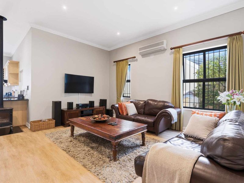 Open-plan living area featuring a wood-burning stove, split-system air conditioning, and laminate flooring, seamlessly connecting to the adjacent kitchen space.