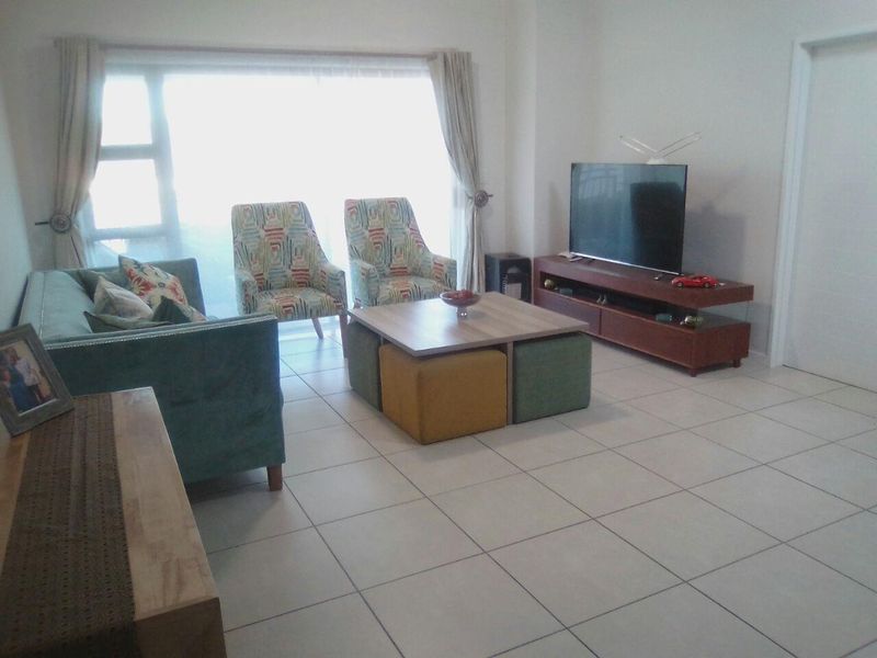 A bright living room featuring neutral tiled flooring and a large sliding glass door providing natural light.