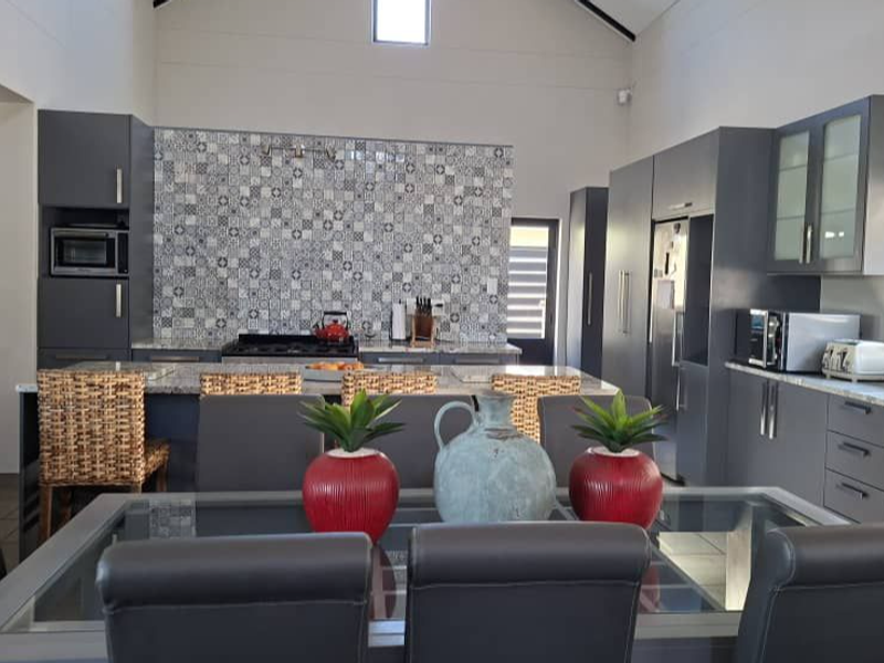 Spacious open-plan kitchen and dining area featuring modern grey cabinetry, stone countertops, a decorative tiled splashback, and a high vaulted ceiling.