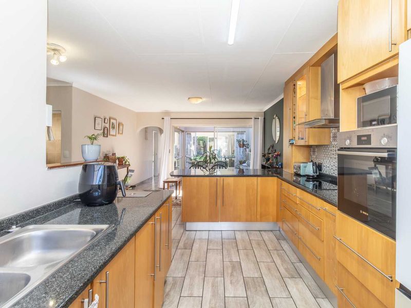 A functional kitchen featuring wood-finish cabinetry, granite countertops, integrated appliances, and tiled flooring, with an open-plan layout leading to the living area.