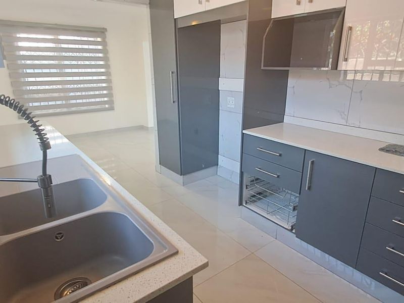 Modern kitchen featuring sleek grey and white cabinetry, quartz countertops, a double bowl sink with gooseneck faucet, and integrated extractor fan.
