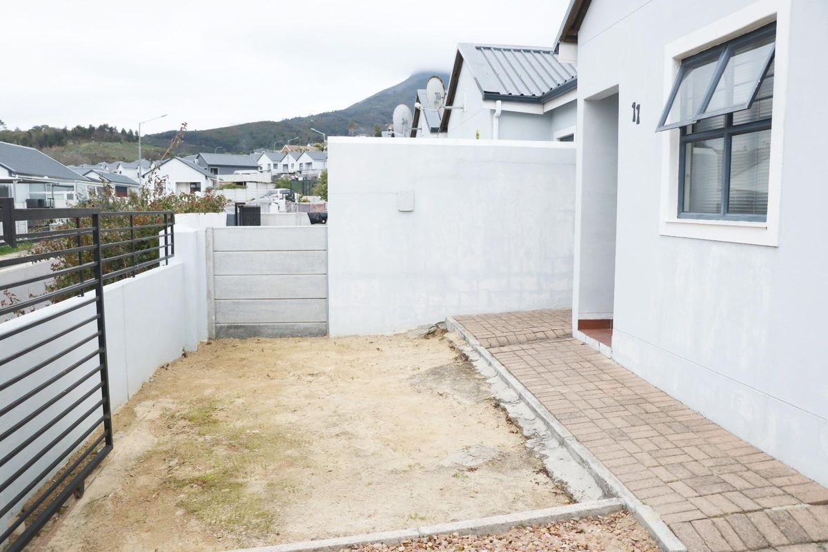 A rear exterior view of the property featuring a paved walkway and an unlandscaped garden area enclosed by boundary walls and fencing.