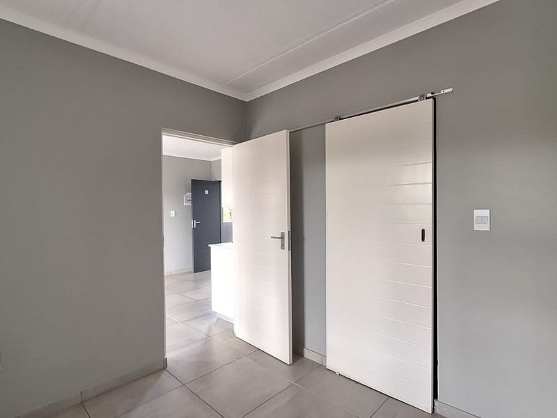 A clean, modern bedroom featuring neutral grey walls, tiled flooring, a sliding door, and built-in cupboard storage.