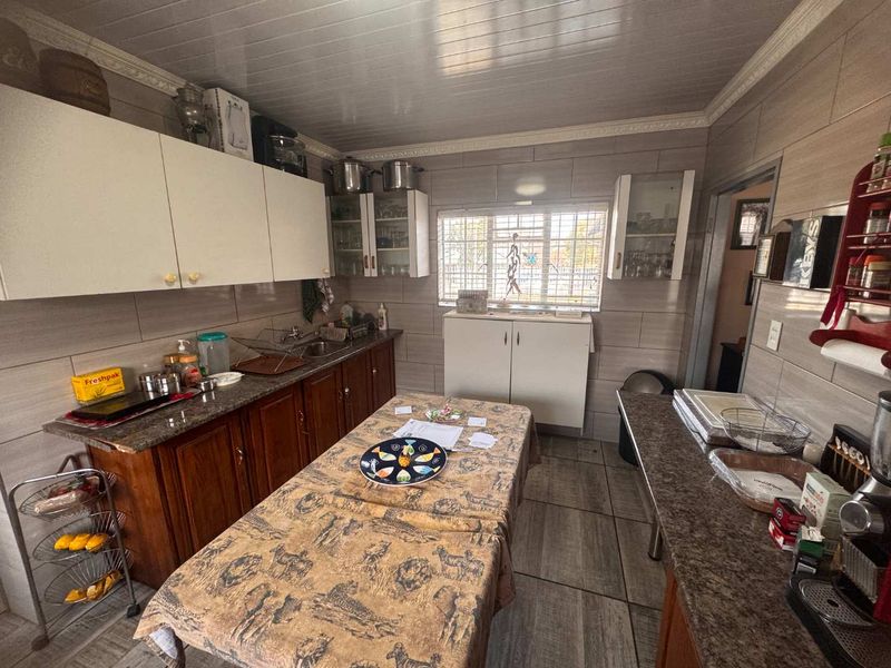 A functional kitchen featuring wood-tone lower cabinetry, white upper cabinets, granite countertops, and tiled wall finishes with a window overlooking the exterior.