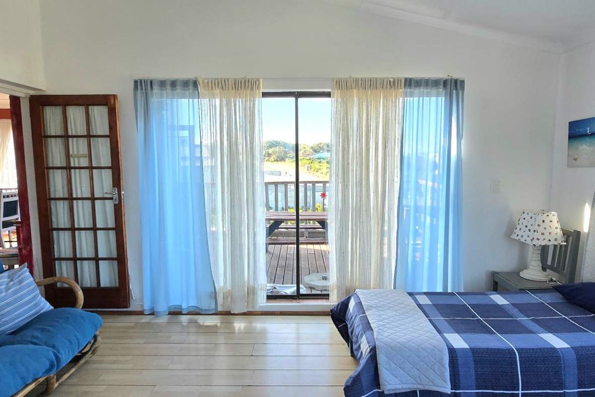 A bedroom featuring timber flooring, a vaulted ceiling, and a sliding glass door providing access to an outdoor deck area.