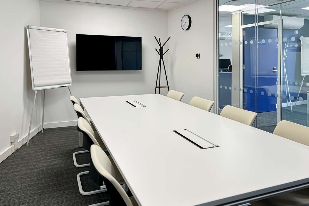 A modern, well-maintained office meeting room featuring a large conference table, glass partition walls, and professional carpet flooring.
