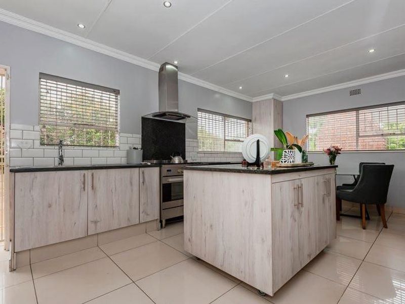 Modern kitchen featuring a central island, stainless steel extractor fan, built-in oven, subway tile backsplash, and light-toned cabinetry with neutral floor tiles.