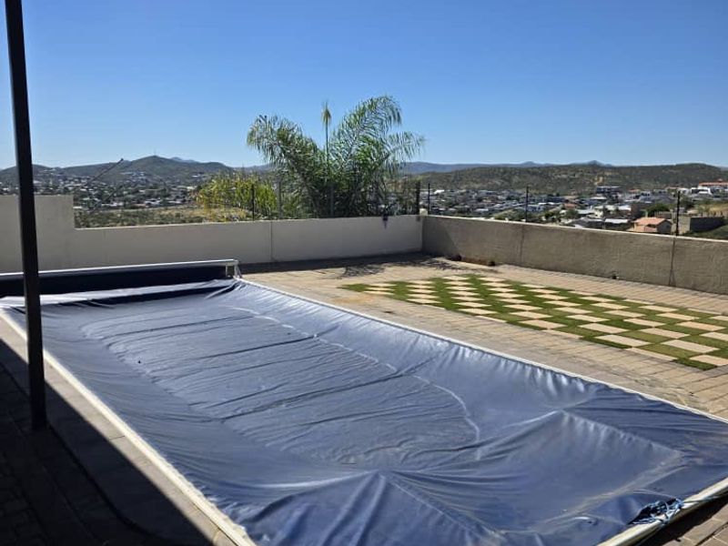 Outdoor pool area featuring a covered patio, paved decking, and a swimming pool with a protective cover, offering expansive elevated views.