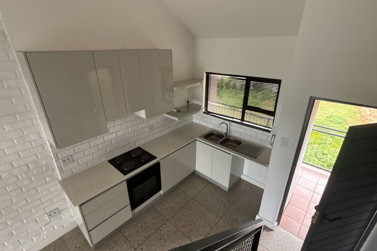 Modern kitchen featuring sleek cabinetry, subway tile backsplash, built-in oven and hob, and direct access to an outdoor balcony area.