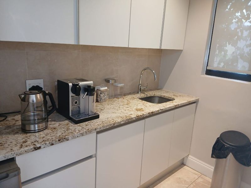 A compact kitchen area featuring modern white cabinetry, granite countertops, and a sleek undermount sink with a chrome mixer tap.