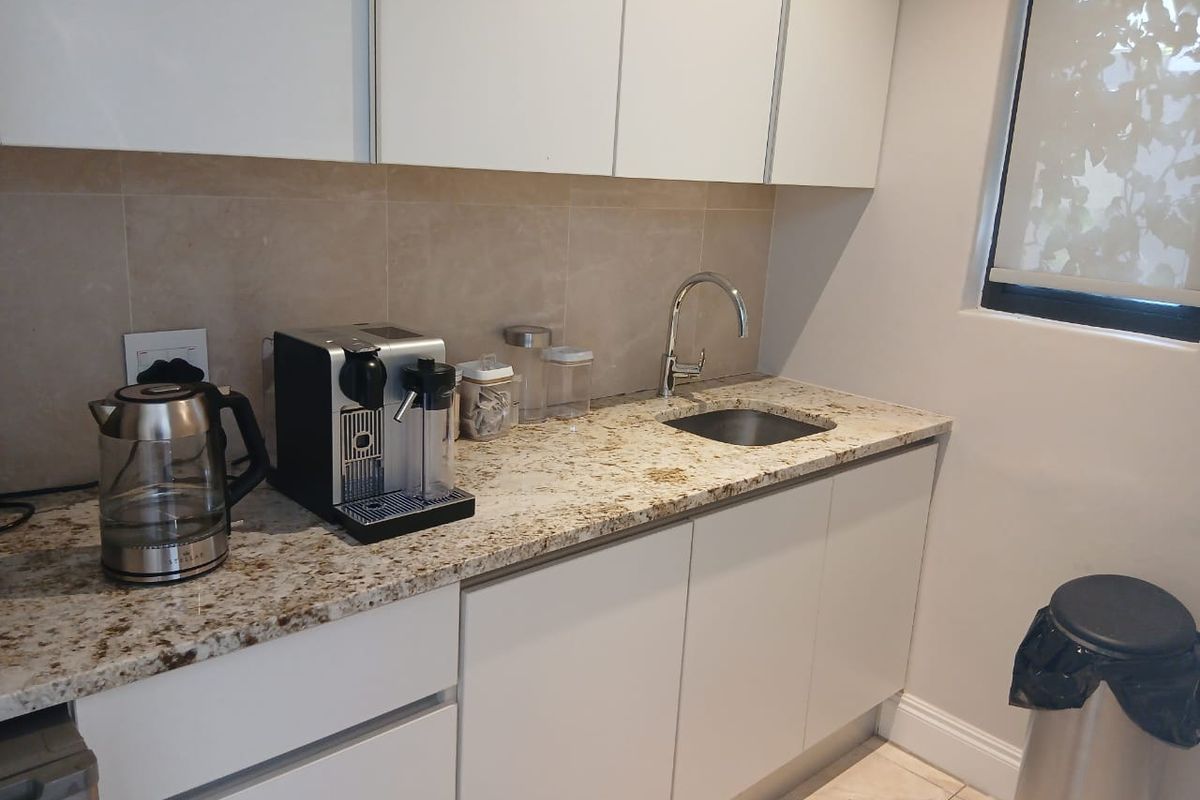 A compact kitchen area featuring modern white cabinetry, granite countertops, and a sleek undermount sink with a chrome mixer tap.