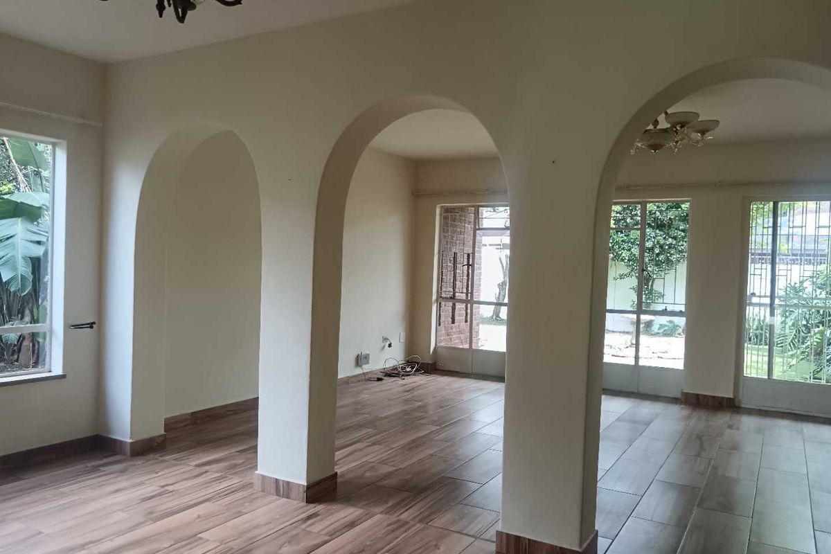 Spacious living area featuring distinctive arched architectural dividers, wood-look tile flooring, and large windows providing ample natural light and garden views.