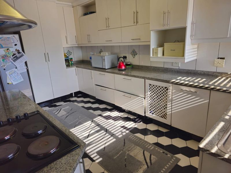 A functional kitchen featuring granite countertops, ample built-in cabinetry, an electric hob with extractor fan, and a distinctive black and white hexagonal tiled floor.