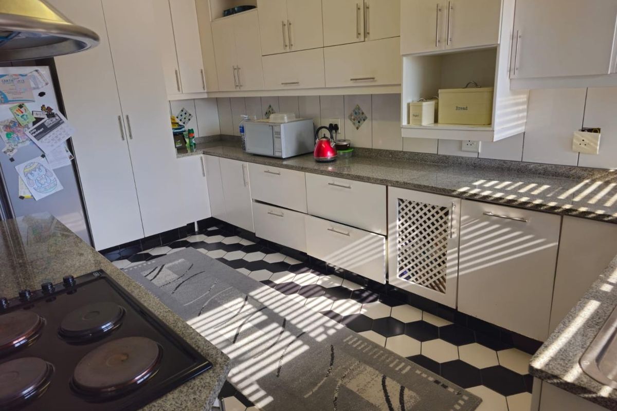 A functional kitchen featuring granite countertops, ample built-in cabinetry, an electric hob with extractor fan, and a distinctive black and white hexagonal tiled floor.