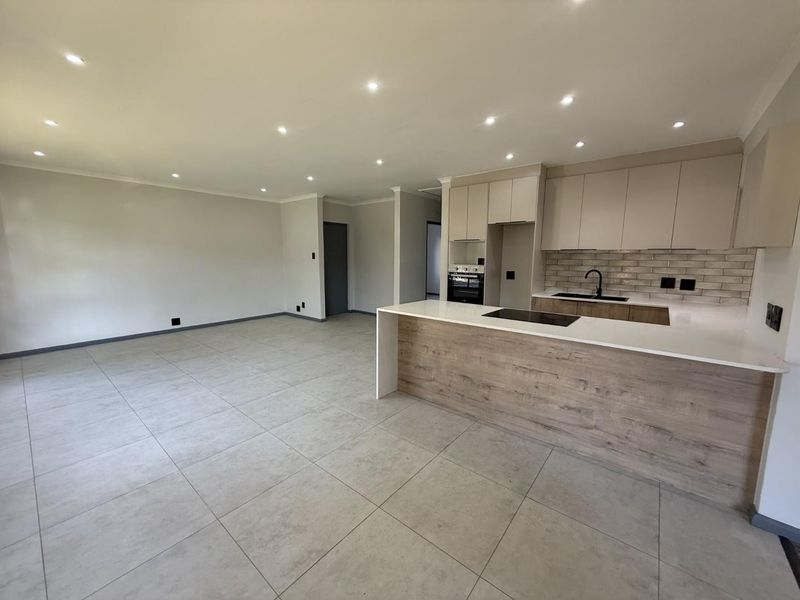 Modern open-plan living area featuring a sleek kitchen with quartz countertops, built-in appliances, and neutral tiled flooring throughout.
